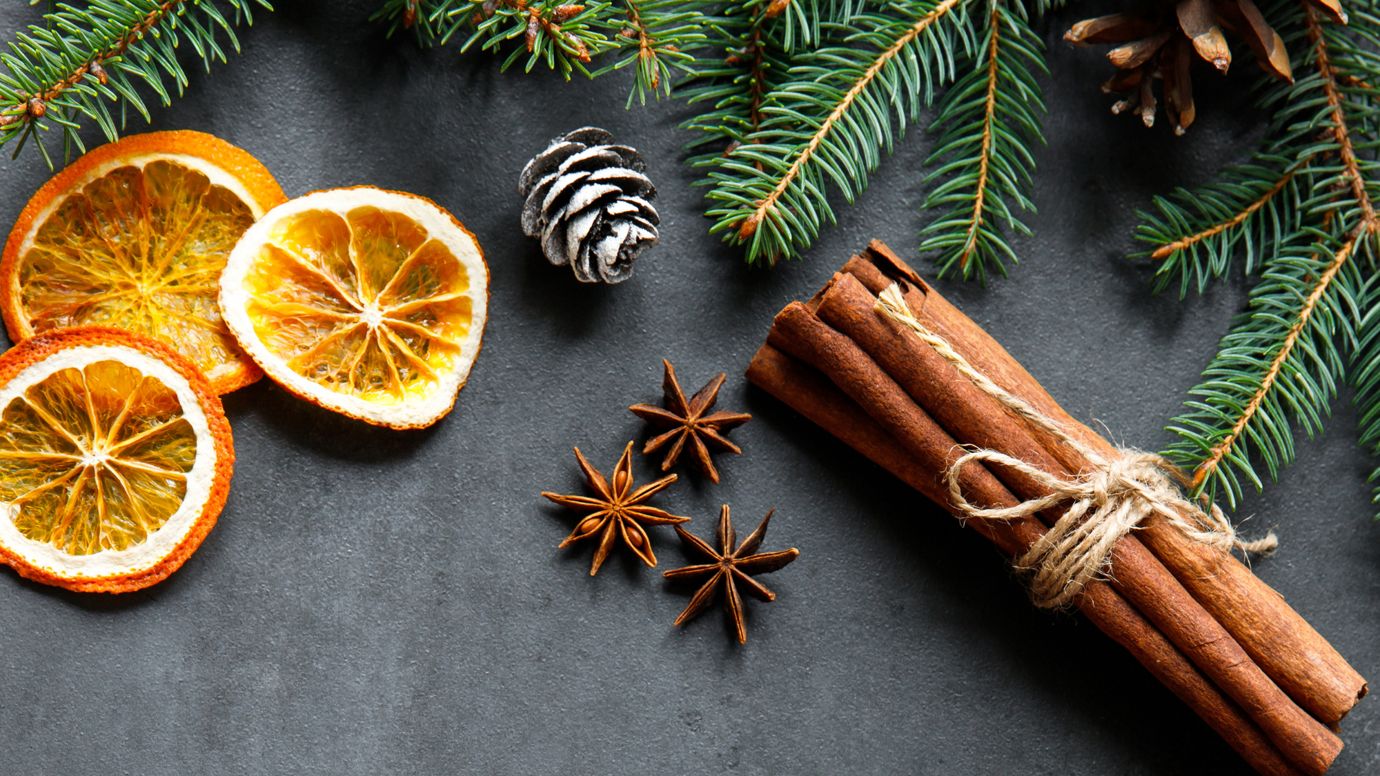 Holiday Simmer Pot Recipe blog post. Scene of holiday spices - orange citrus slices, star anise, cinnamon sticks, pine branches, and pinecones.