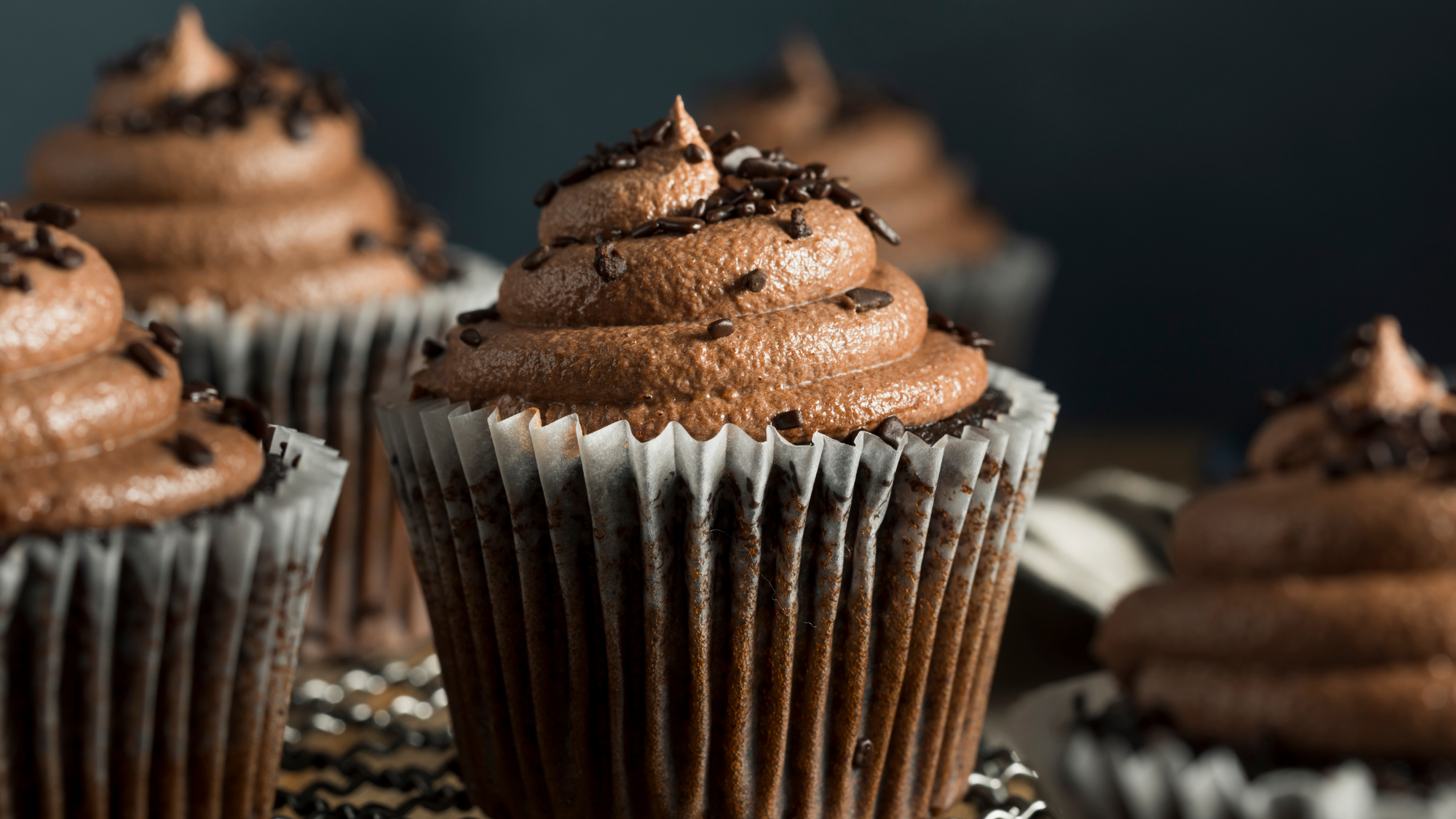 One Bowl Chocolate Cupcakes Recipe blog post. A plate of chocolate cupcakes with chocolate buttercream and sprinkles.