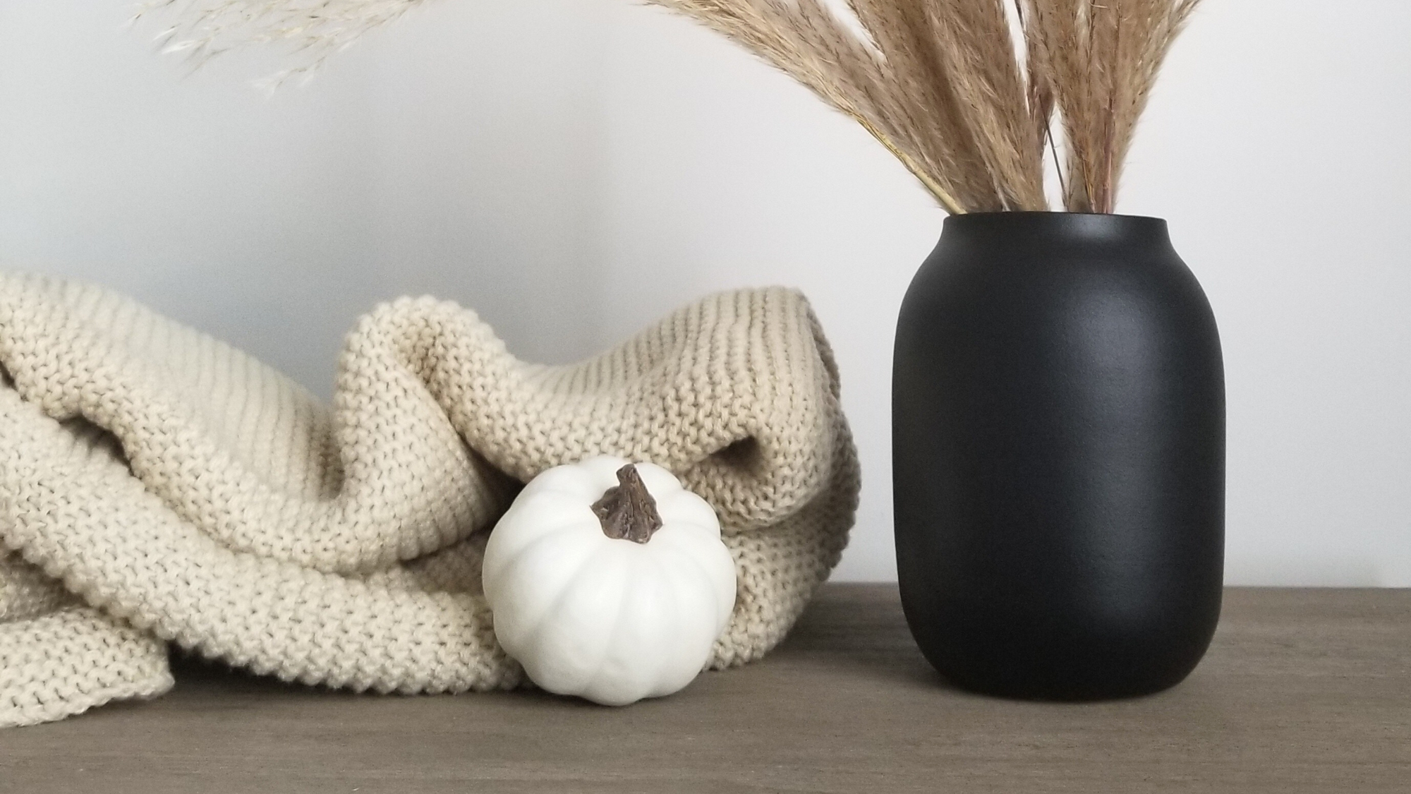 6 Easy Ways to Transition Your Home Decor For Fall blog post. Scene of black vase with pampas grass, cozy neutral blanket, and white pumpkin decor.